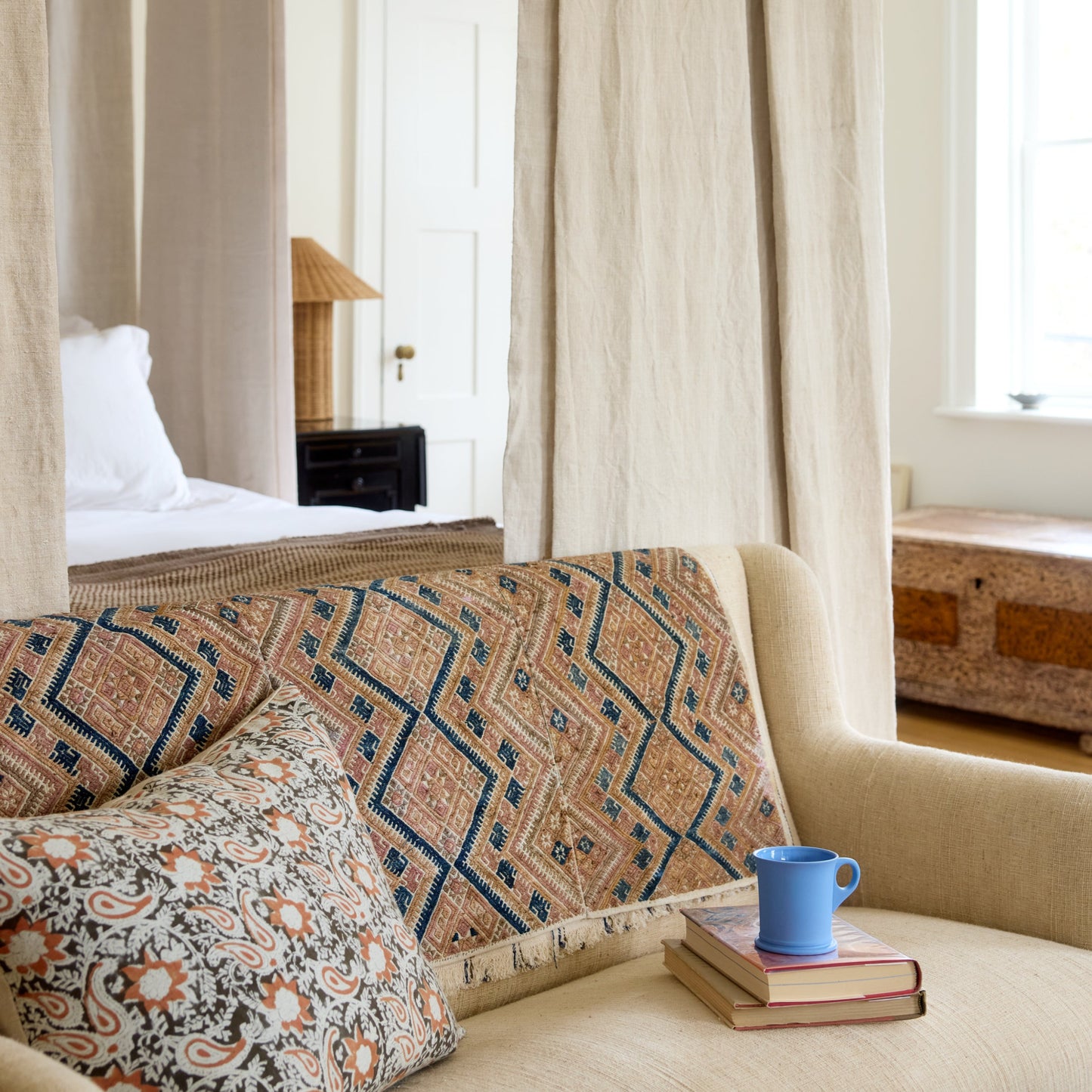 Decorative sofa with patterned cushions and a blue mug in a room with curtains and a mirror.