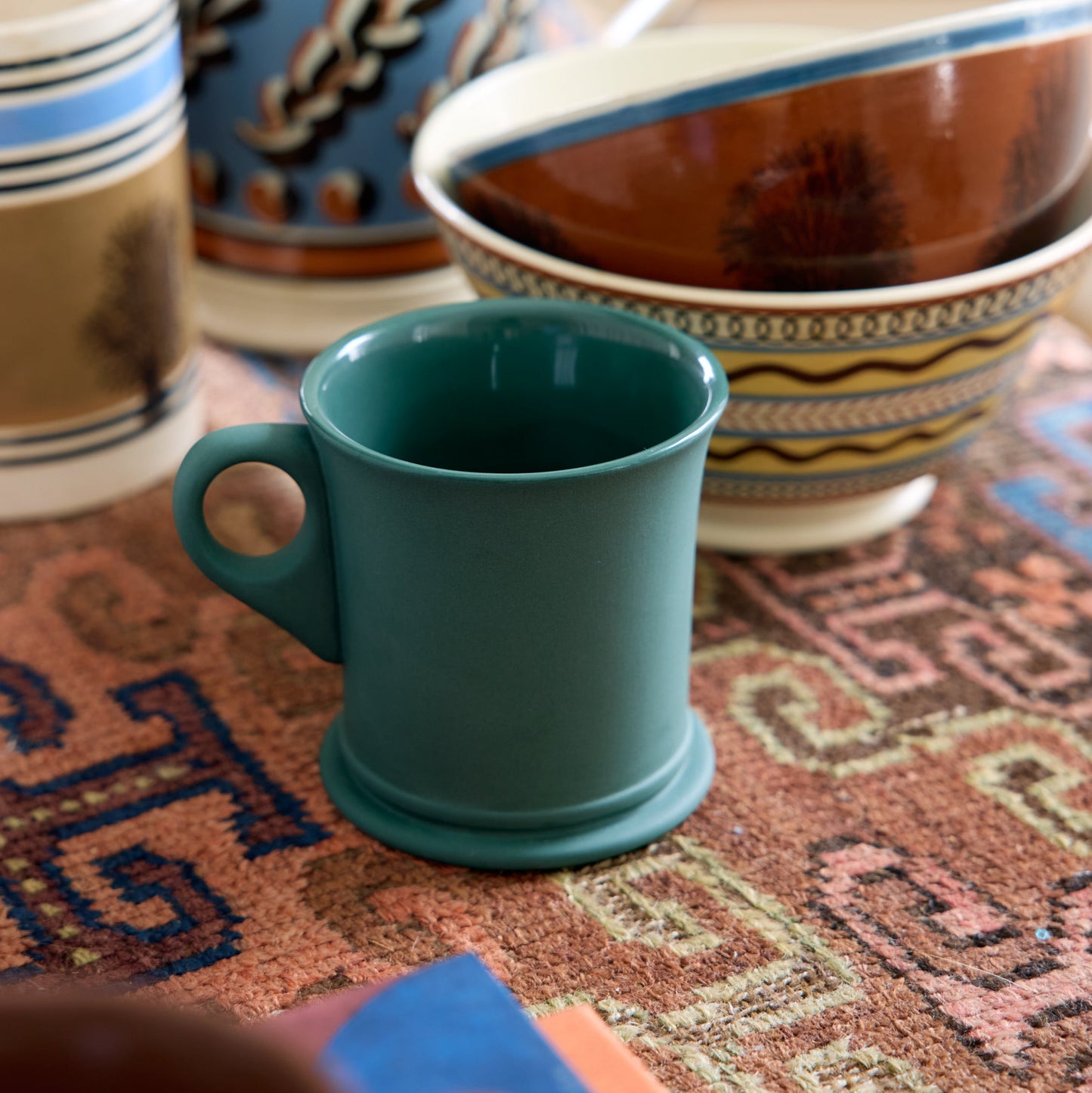 Teal mug on a patterned surface with ceramic items in the background