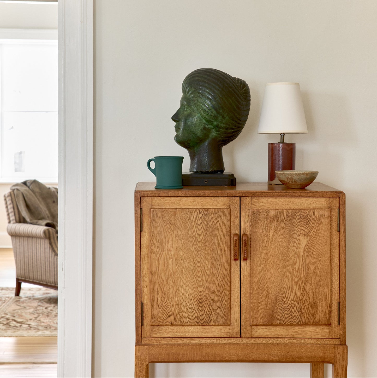 Wooden cabinet with decorative items including a bust and lamp in a room setting.