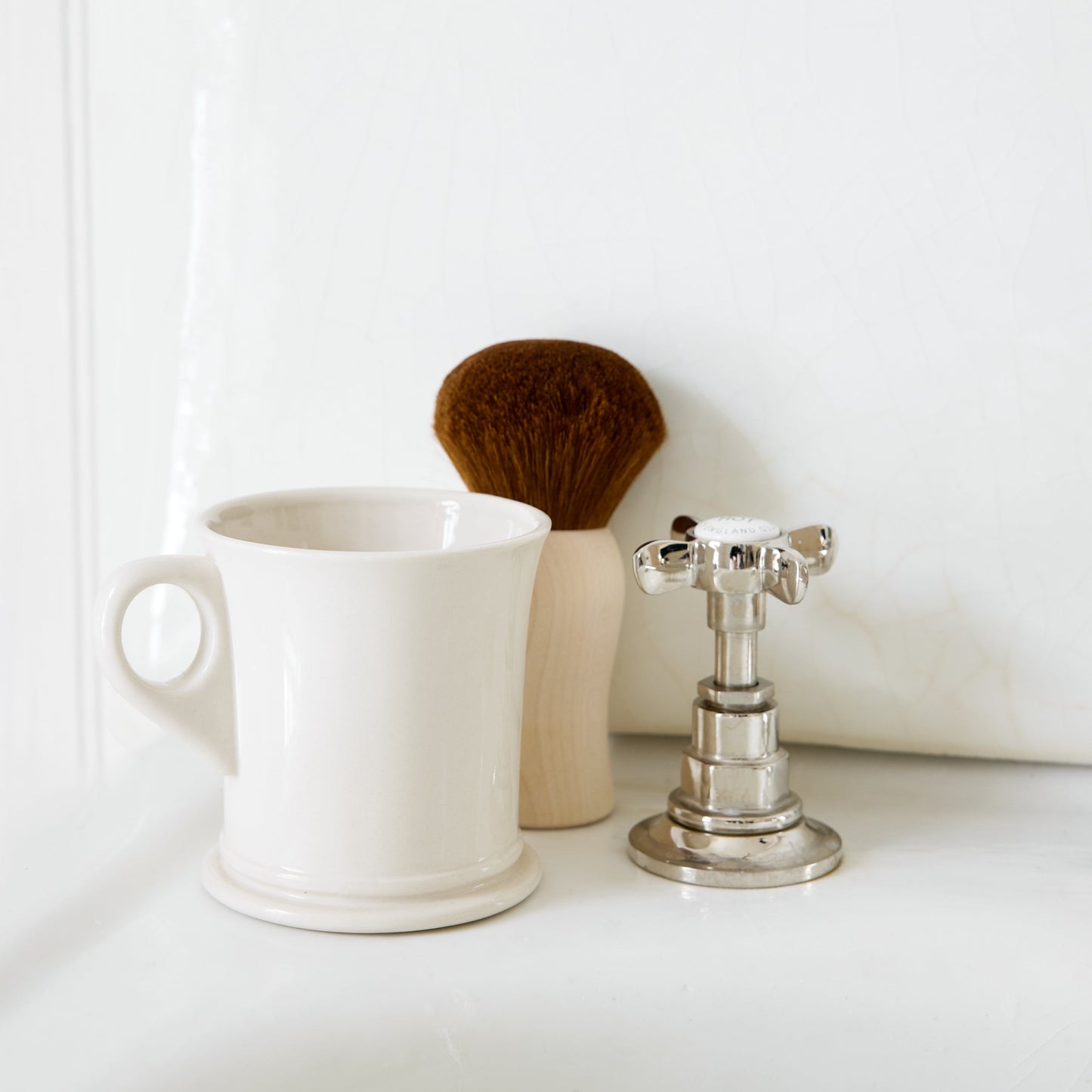 White mug, brush, and silver candle holder on a white surface with a white background