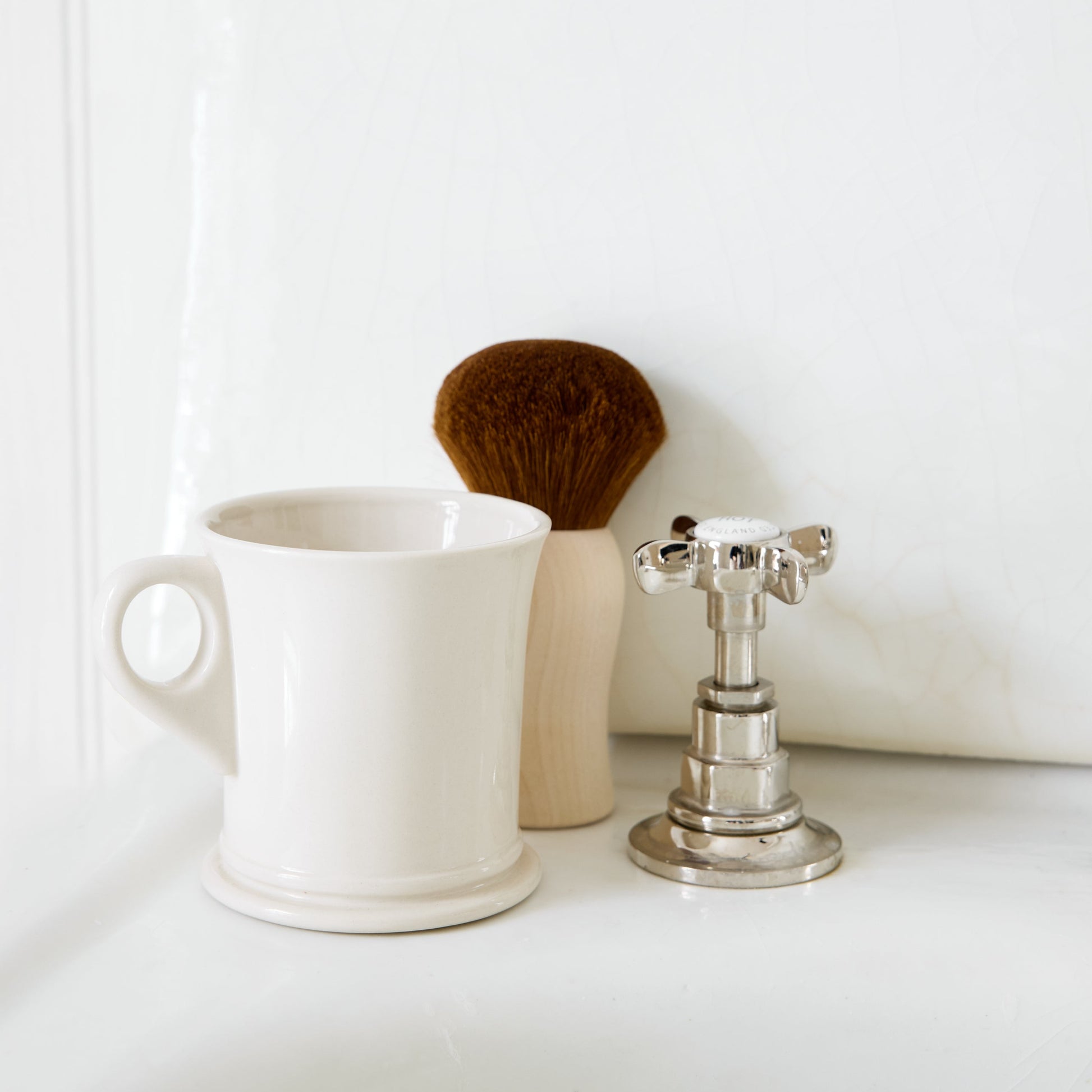 White mug, brush, and silver candle holder on a white surface with a white background
